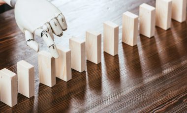 robotic hand picking wooden brick from row of blocks on desk with copy space