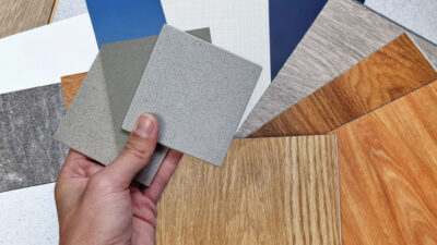 interior designer's hand holding quartz stone samples matching color with wood vinyl flooring tiles, engineering wood tiles, stone tiles, solid color laminateds, artificial stone tiles. close up view.