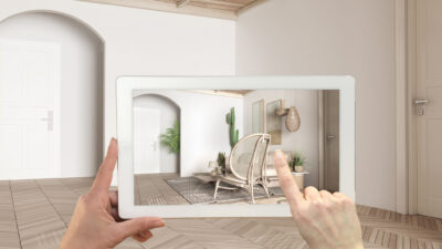 Augmented reality concept. Hand holding tablet with AR application used to simulate furniture and design products in empty interior with parquet, modern living room with sofa