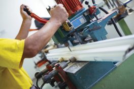 Close up photo of workers hands doing some job on big metalworking machine. Selective focus. Factory for production aluminium and PVC windows and doors.