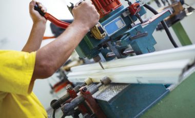 Close up photo of workers hands doing some job on big metalworking machine. Selective focus. Factory for production aluminium and PVC windows and doors.