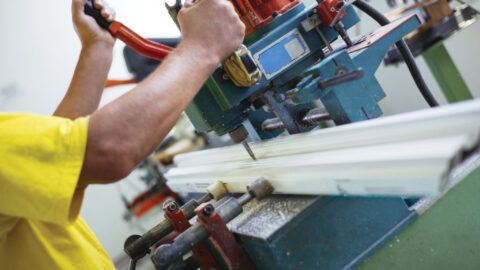 Close up photo of workers hands doing some job on big metalworking machine. Selective focus. Factory for production aluminium and PVC windows and doors.