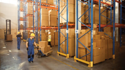 Retail Warehouse full of Shelves with Goods in Cardboard Boxes, Workers Scan and Sort Packages, Move Inventory with Pallet Trucks and Forklifts. Product Distribution Delivery Center.